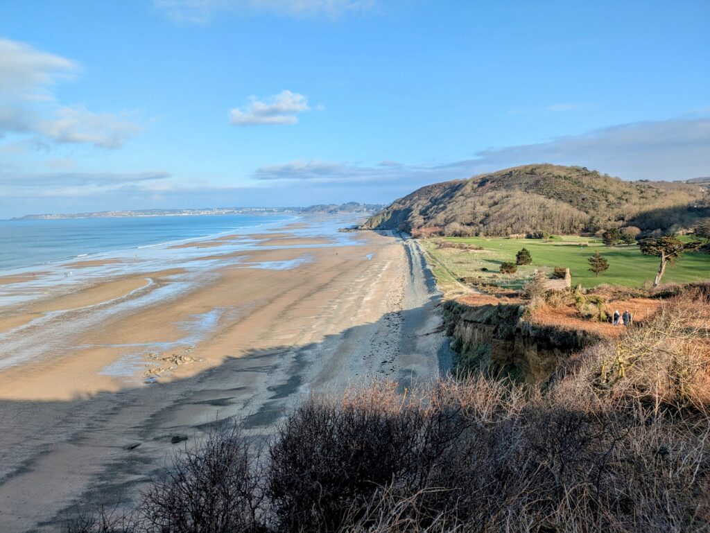 Photo d'une plage de bretagne, prise depuis le sentier des douaniers qui longe les falaises surplombant la plage. Le ciel est bleu et le soleil est bien présent, mais les couleurs de la photo font ressentir qu'il ne devait pas faire chaud ce jour-là.