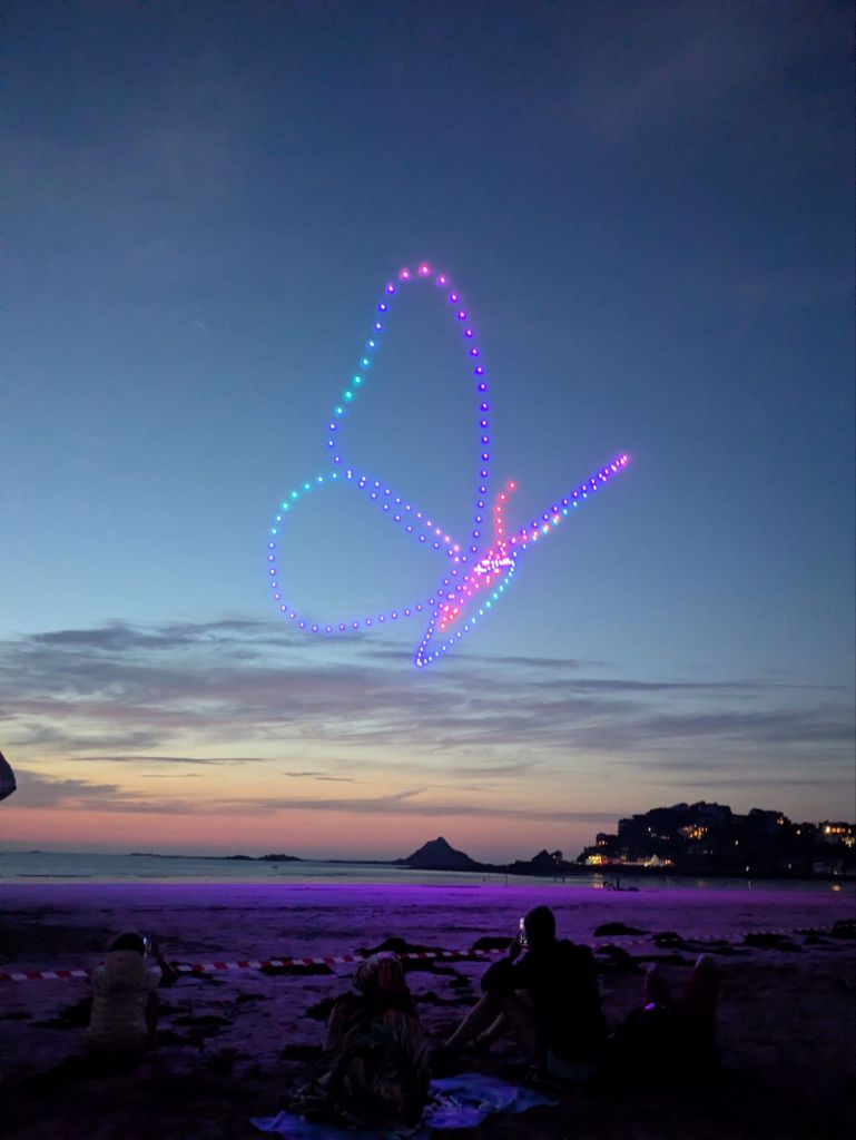 A group of drones flying above a beach at night, forming the shape of a butterfly 